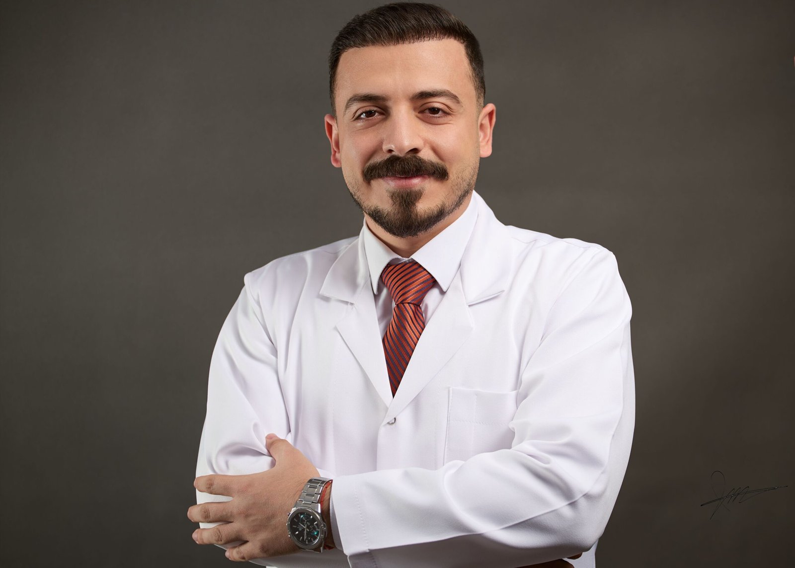 Confident doctor in a white coat with red tie, standing with crossed arms.